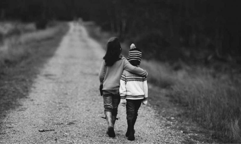 Two children walking down a quiet dirt road with their arms around each other, capturing the theme of the best friendship movies in 2026.